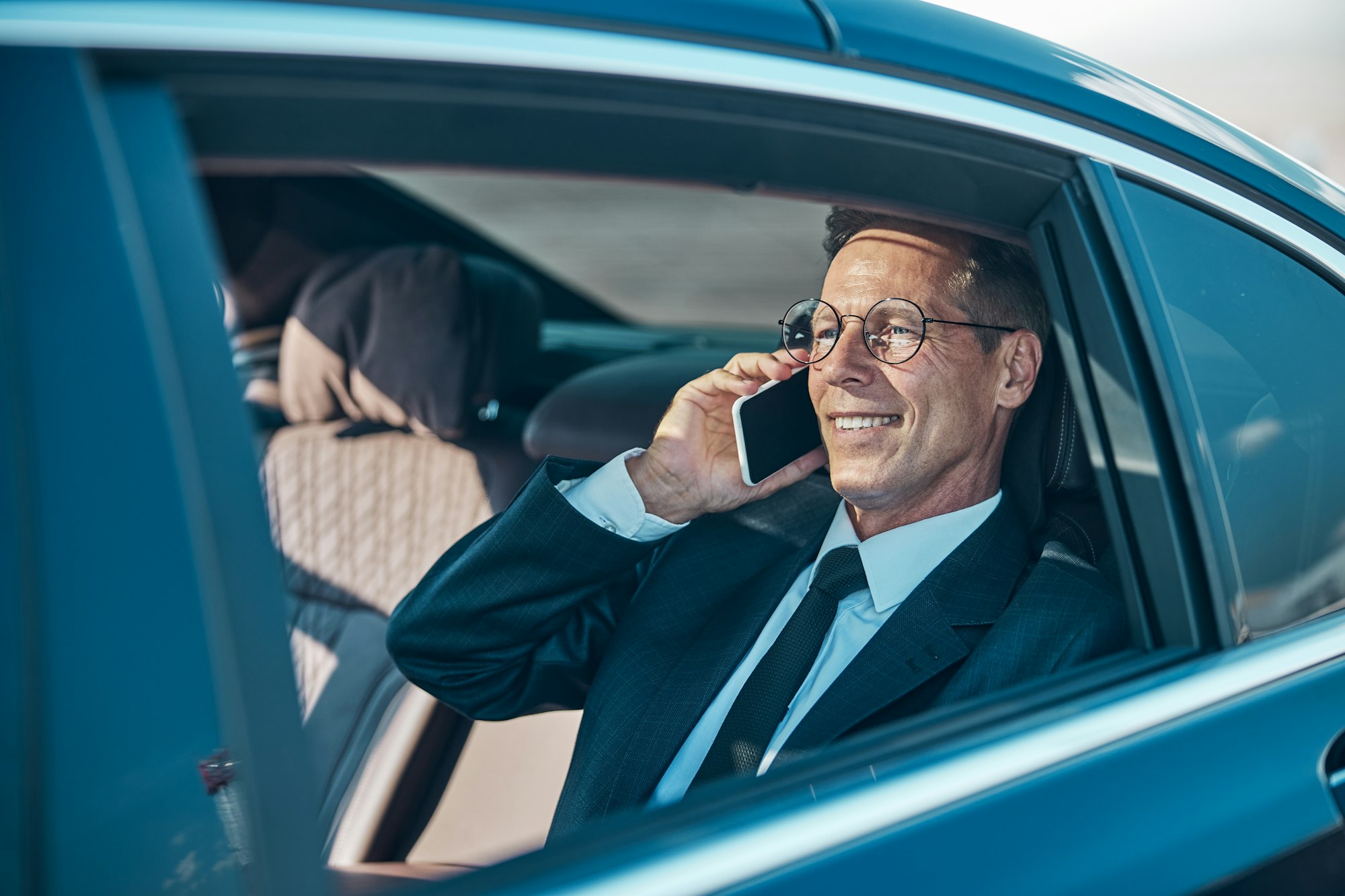 Cheerful businessman talking on smartphone during transfer from airport Cheerful businessman talking on smartphone during transfer from airport